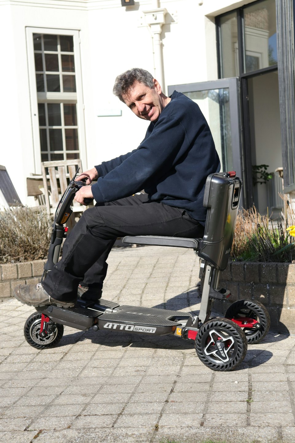 Ein Mann mit grauen Haaren lächelt, während er auf seinem Elektrorollstuhl fährt.